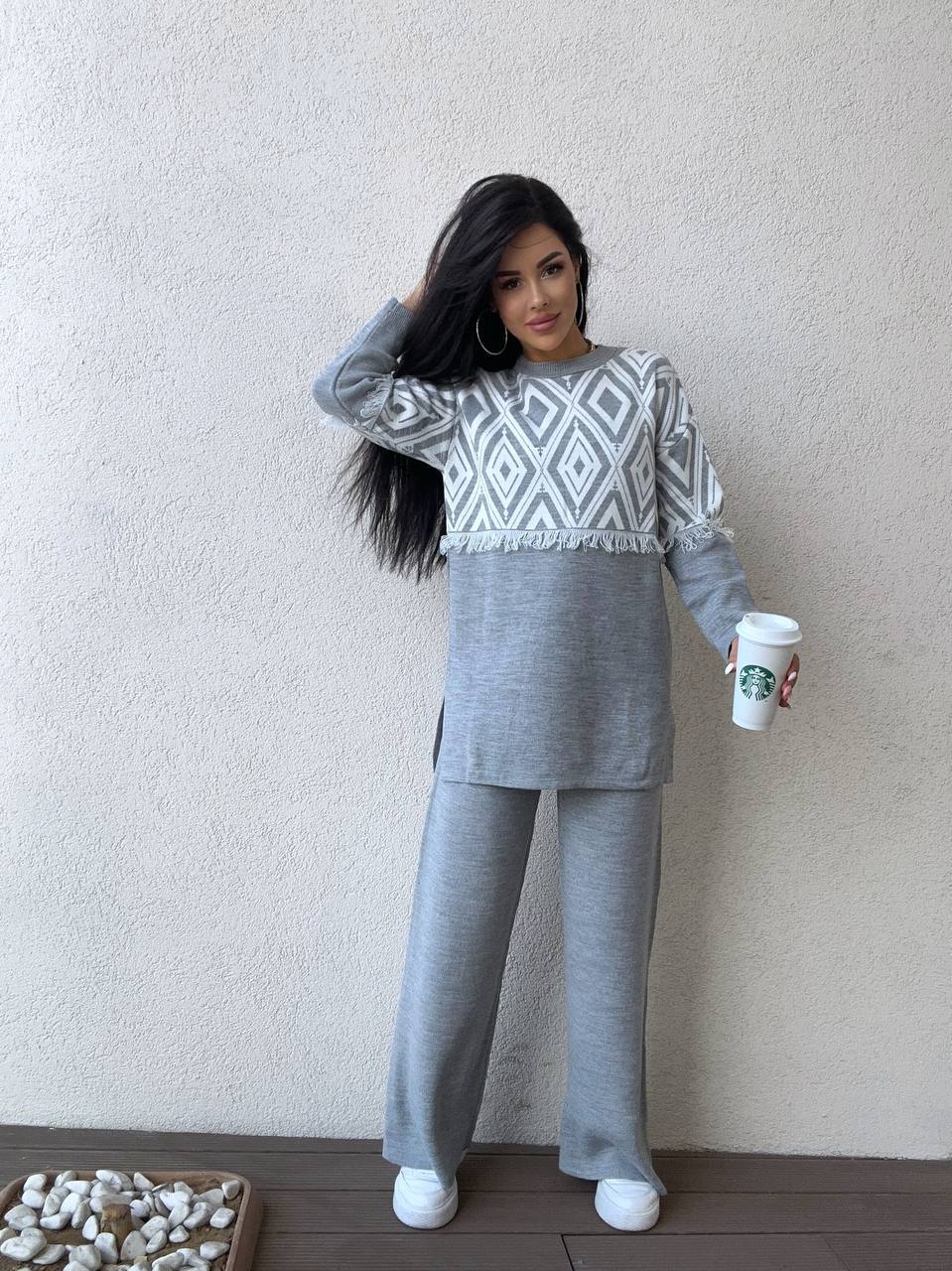 Woman in gray outfit holding a white cup against a plain wall