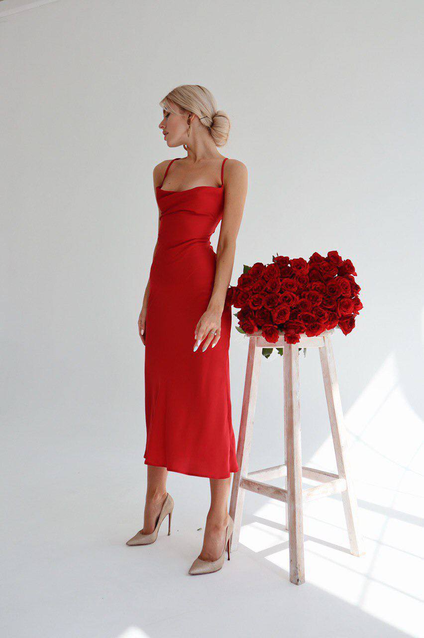 Woman in a red dress standing next to a tall wooden stool with red roses against a white background