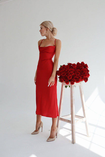 Woman in a red dress standing next to a tall wooden stool with red roses against a white background