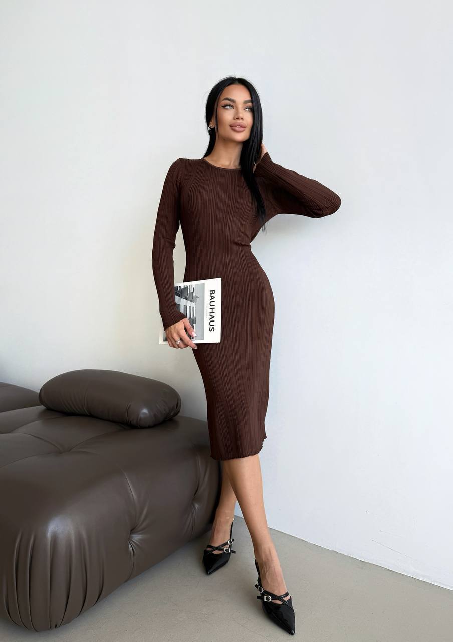 Woman in a brown dress holding a magazine in a minimalistic room.