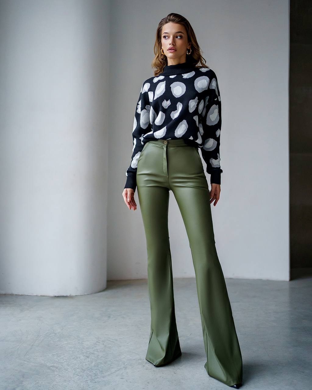 Woman wearing a patterned sweater and green pants against a neutral background