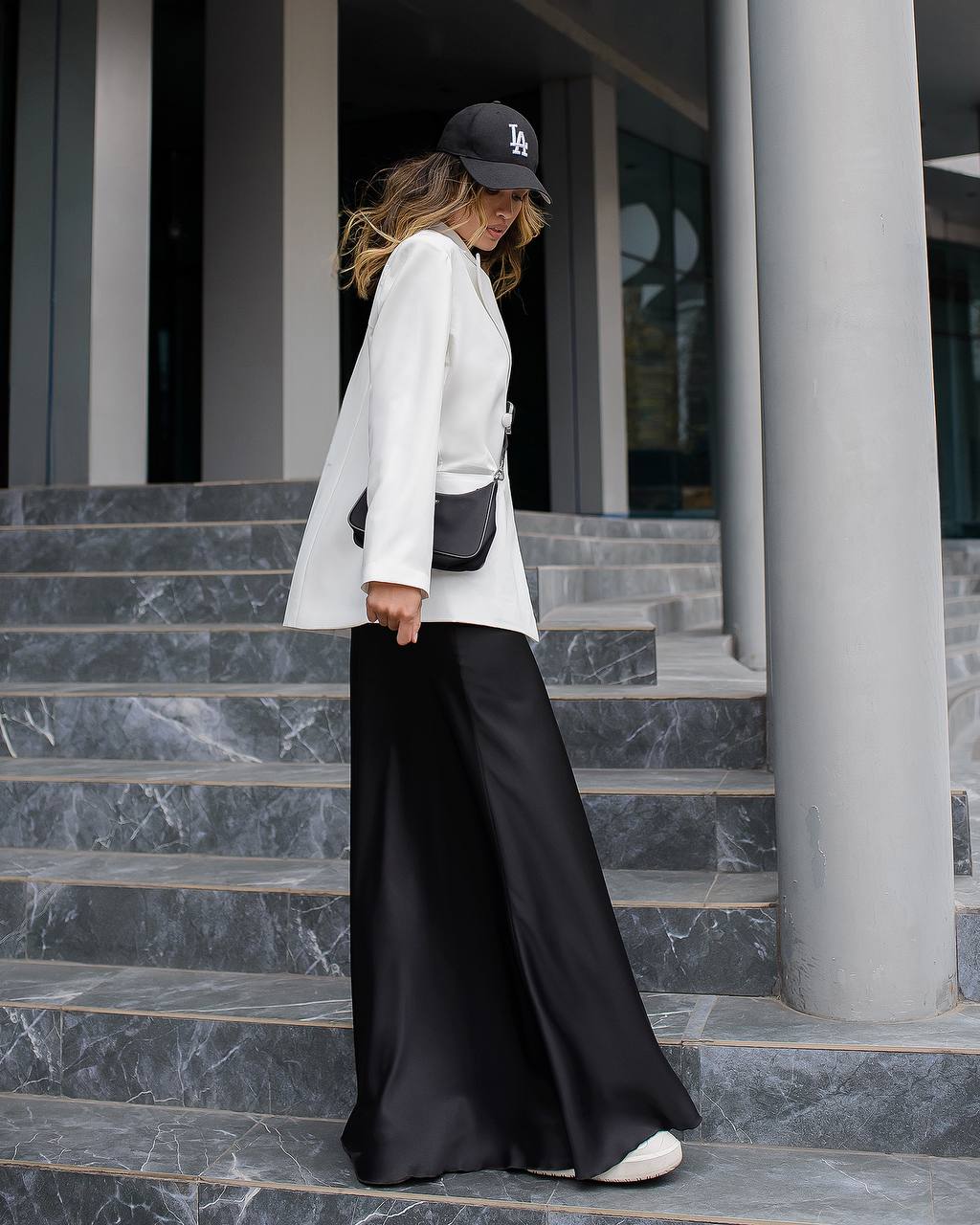 Woman in white blazer and black pants standing on marble steps.