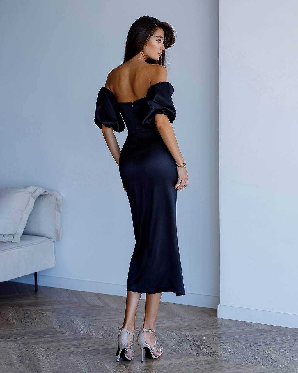 Woman wearing a black off-shoulder dress in a minimalistic room.