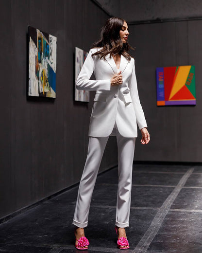 Woman in a white suit standing in an art gallery with colorful paintings on the wall.