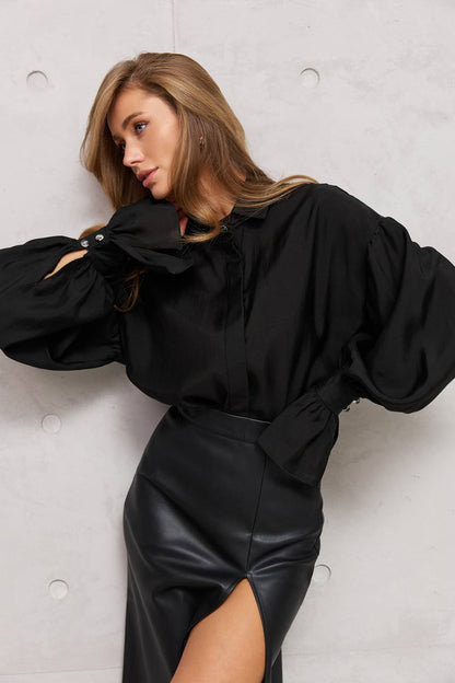 Woman wearing a black outfit with a high collar and leather skirt against a light gray background