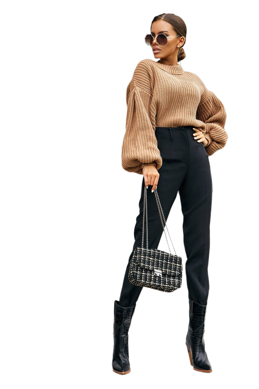 Woman wearing a beige sweater, black pants, and black boots holding a patterned handbag on a white background