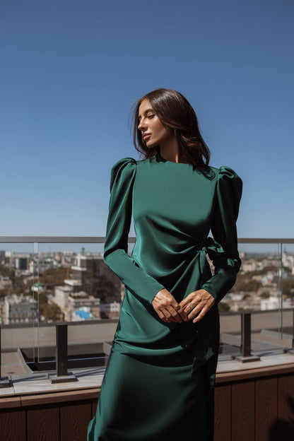 Woman in a green dress standing on a rooftop with a cityscape in the background