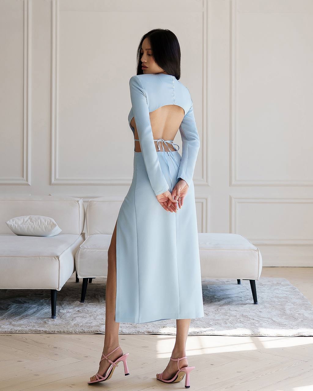 Woman wearing a light blue dress with an open back in a room with white walls and furniture.
