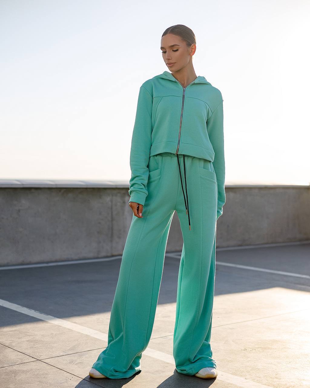 Person wearing a teal tracksuit standing on a rooftop with a clear sky.
