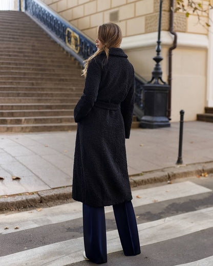 Woman in a long black coat walking on a city street.