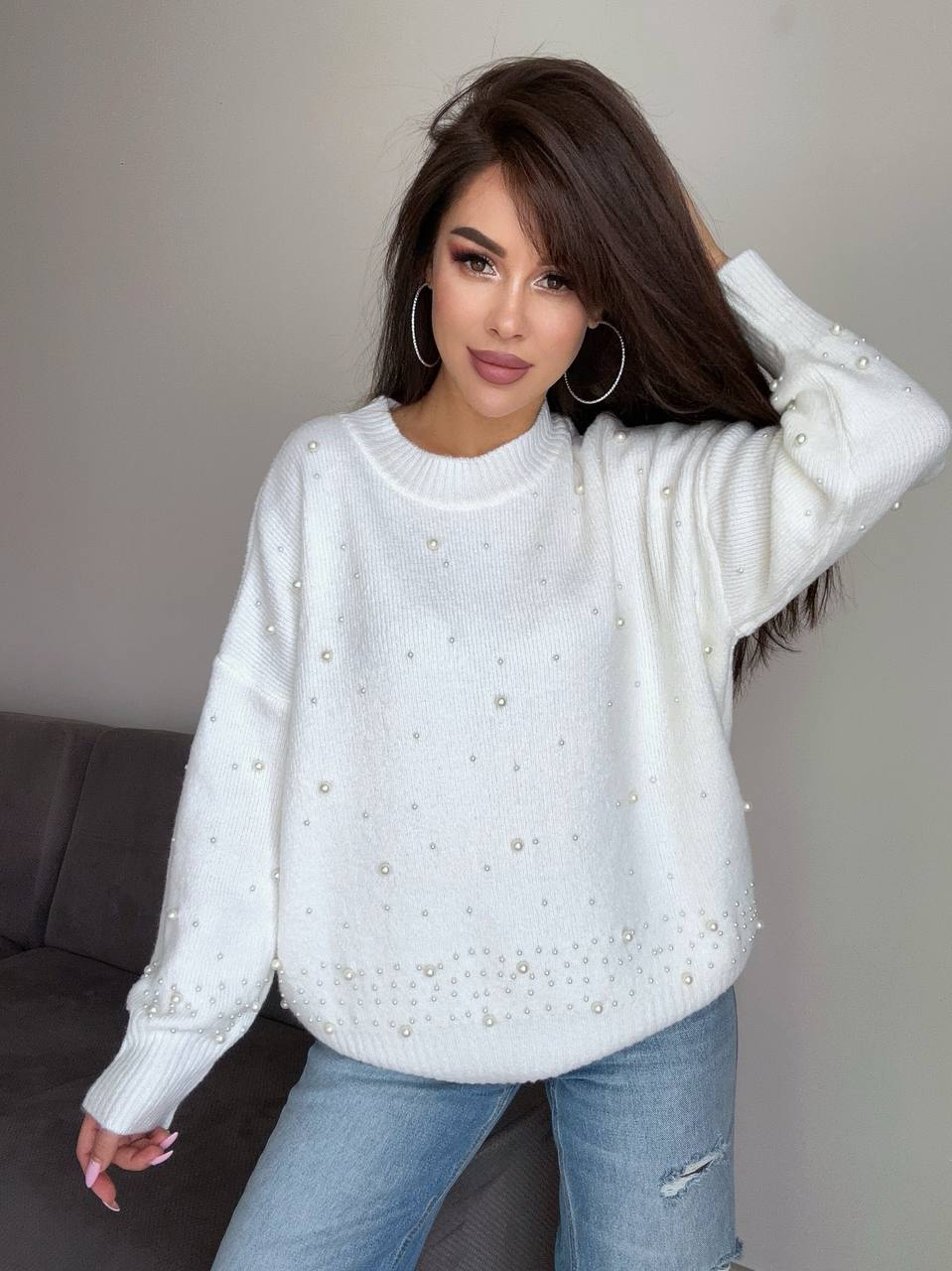 Woman wearing a white sweater with pearl embellishments against a neutral background