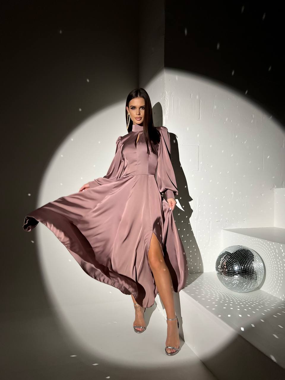 Woman in a pink dress standing in a spotlight with a disco ball in the background