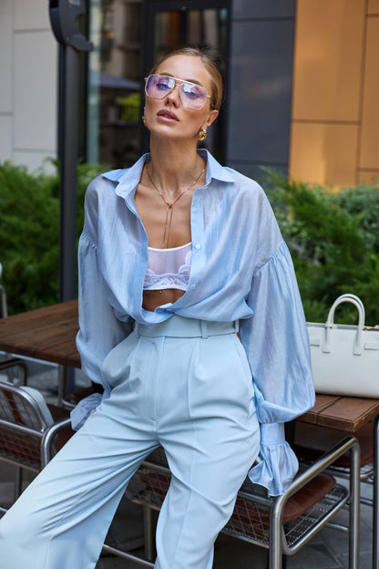 Woman in light blue outfit with sunglasses sitting outdoors