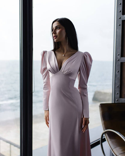 Woman in a pink dress standing by a large window with a view of the ocean.