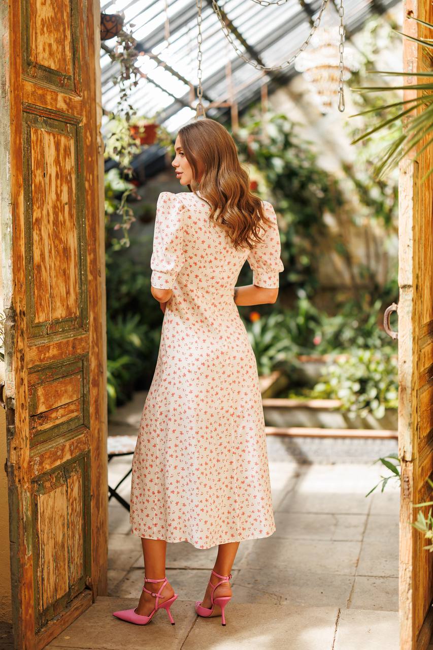 Woman in a floral dress standing in a greenhouse with large wooden doors.
