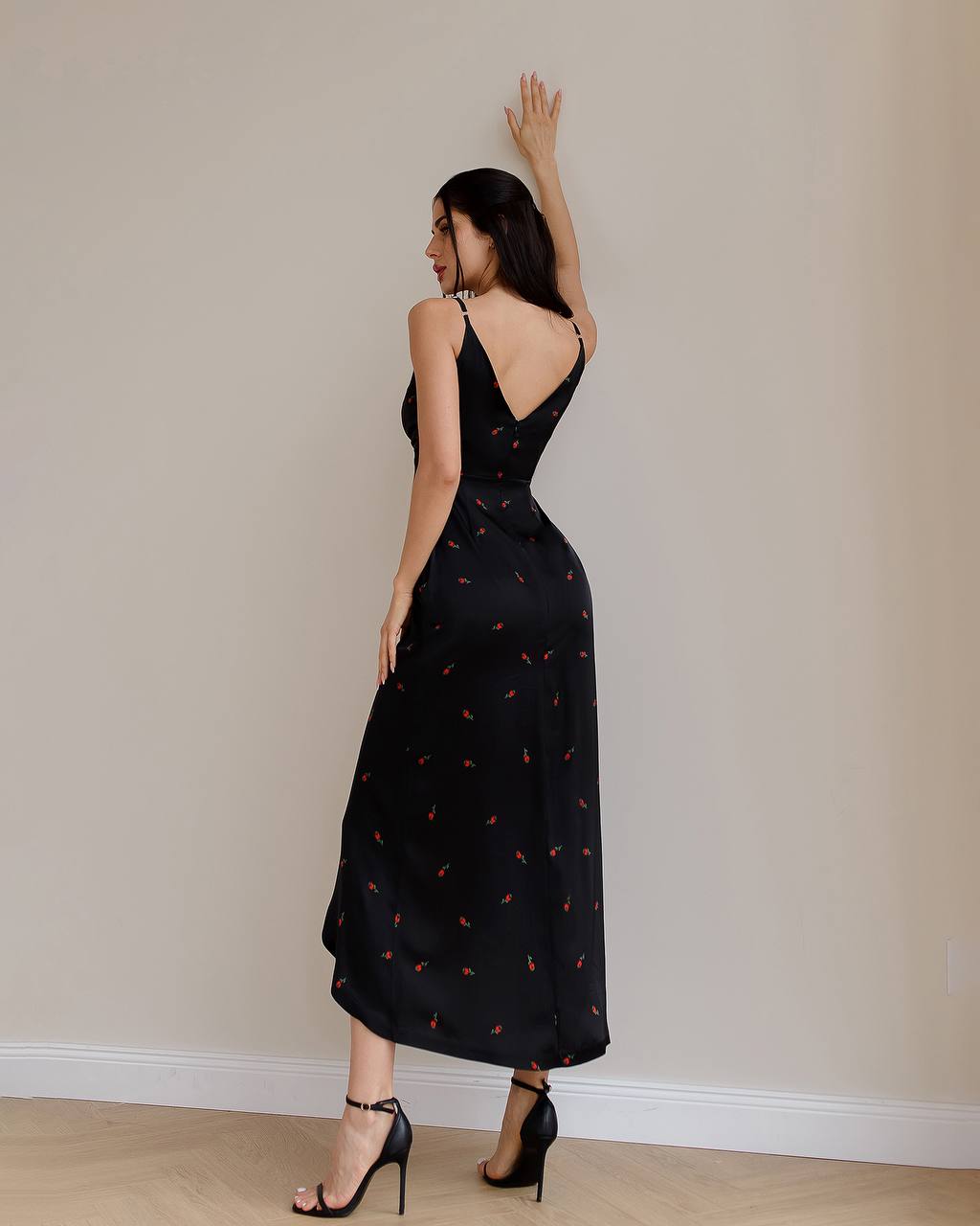 Woman wearing a black dress with a subtle pattern, standing against a plain wall.