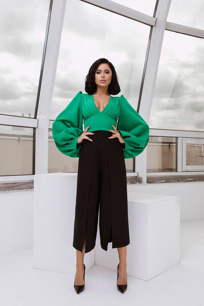 Woman wearing a green blouse and black pants in a modern indoor setting