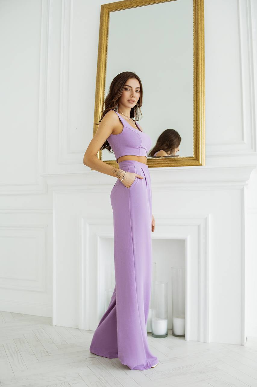 Woman in a lavender dress standing in front of a mirror in a white room.