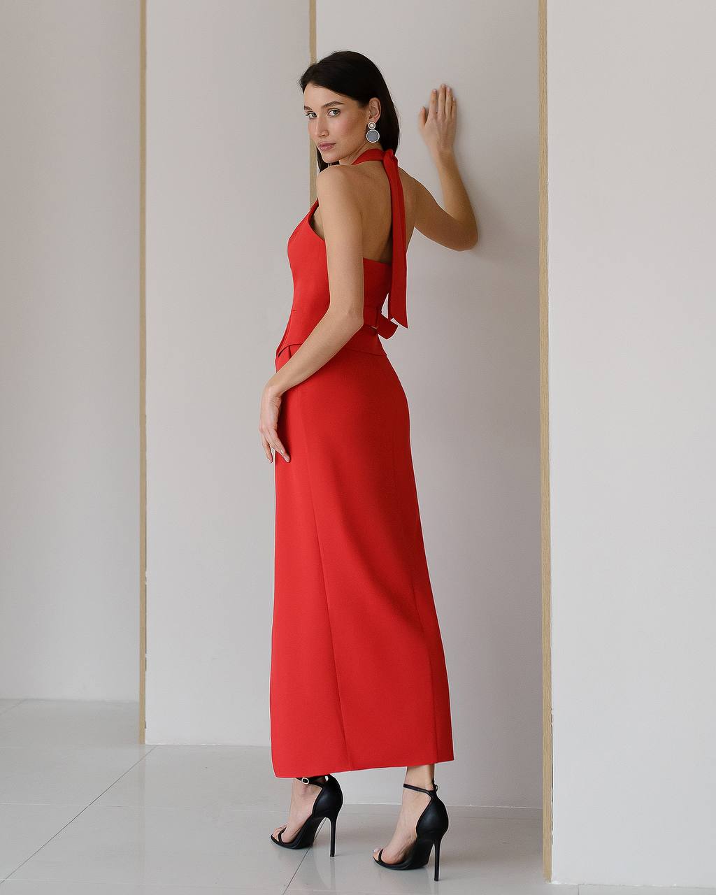 Woman in a red dress standing against a plain wall.