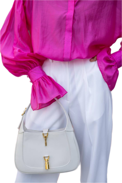 Person wearing a bright pink blouse and white pants holding a light gray handbag with gold accents.