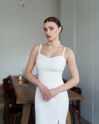 Woman in a white dress standing in a room with wooden furniture.