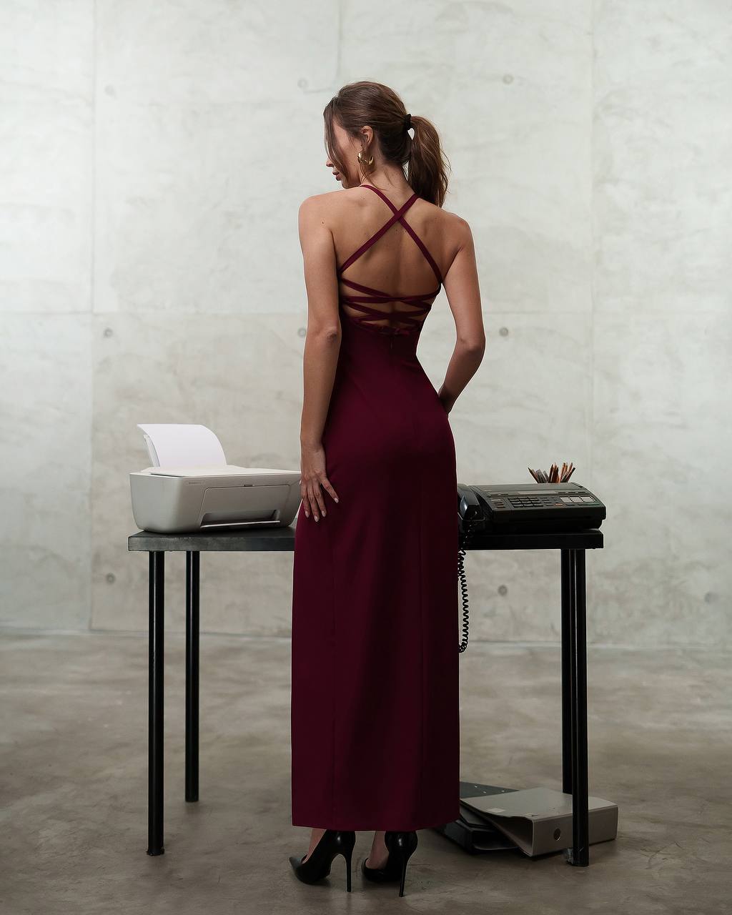 Woman in a burgundy dress standing in front of a desk with office equipment.