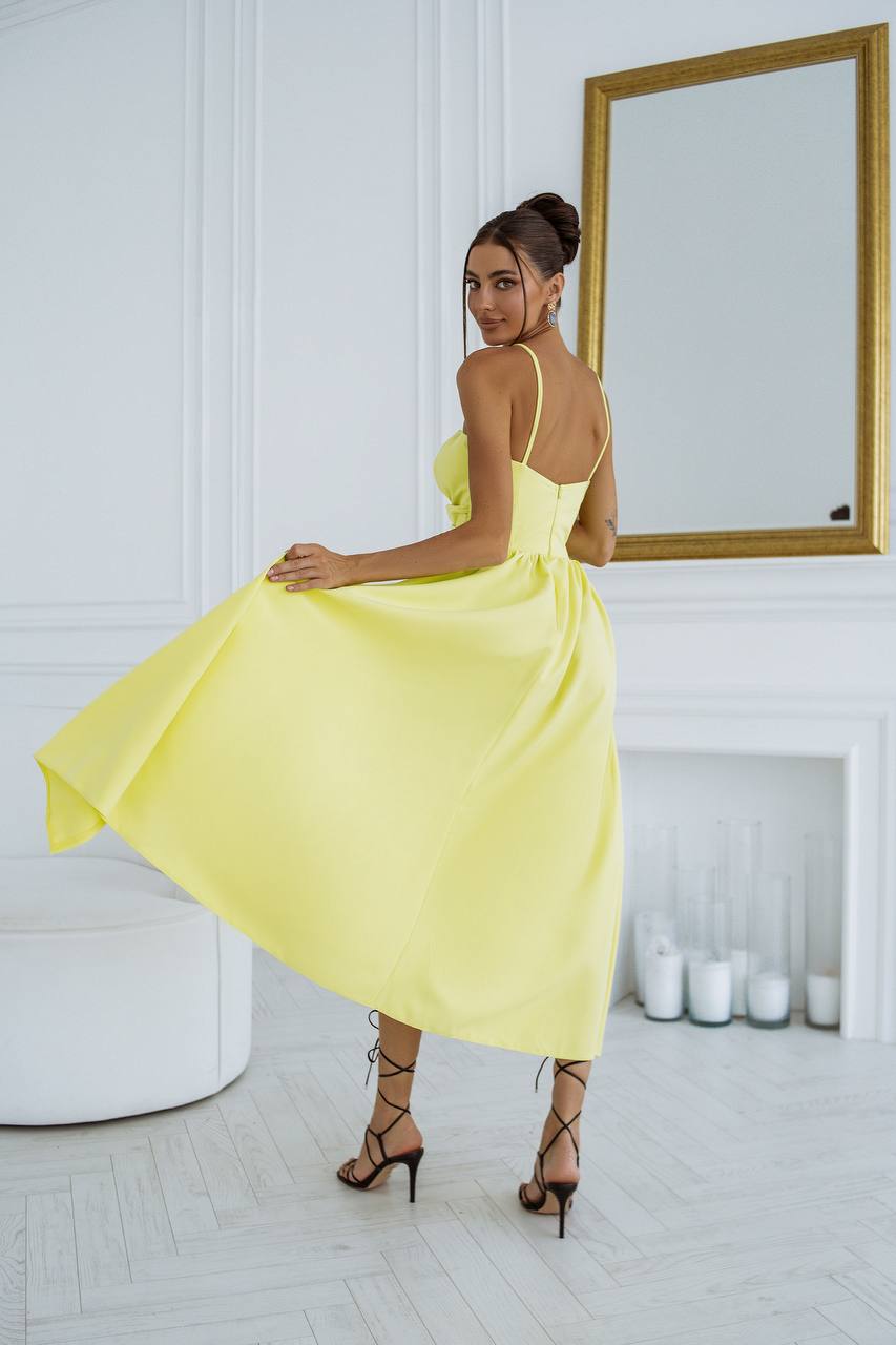 Woman in a yellow dress standing in a room with a mirror and white walls.
