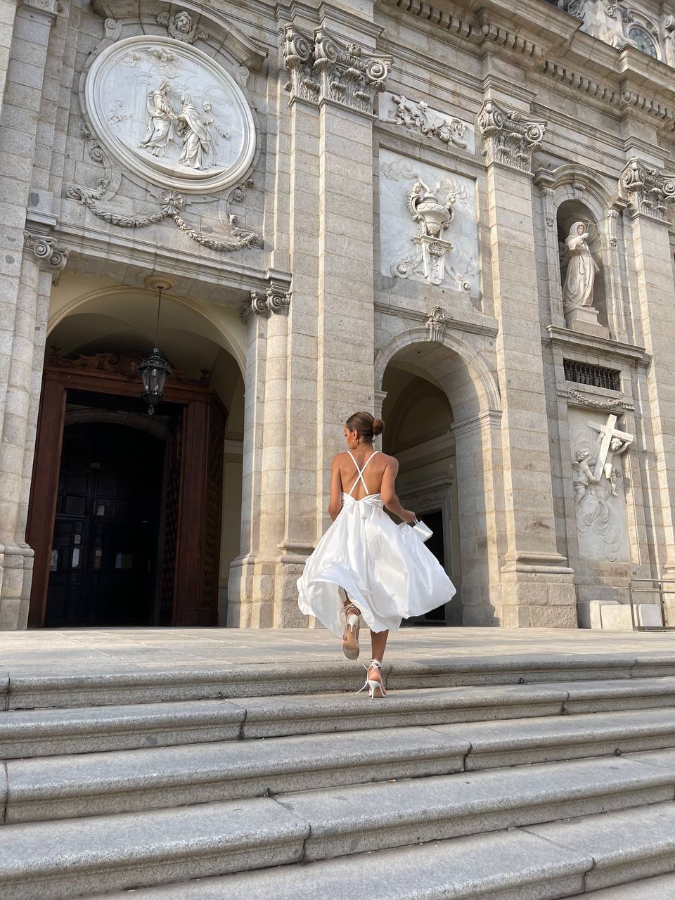 Woman in a white dress walking up steps in front of an ornate building
