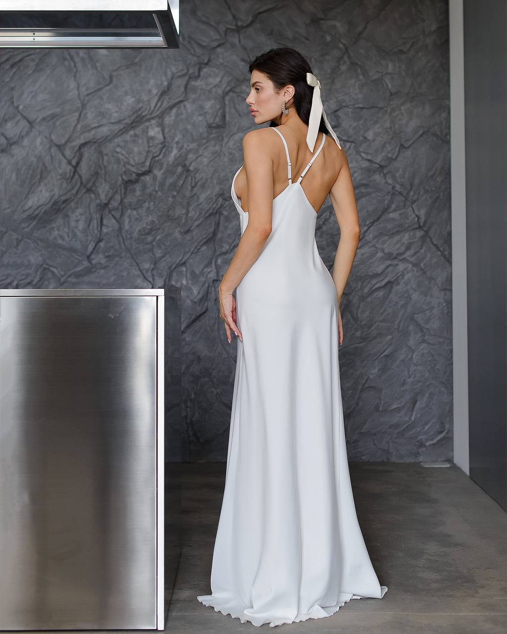 Woman in a white dress standing against a dark textured wall.