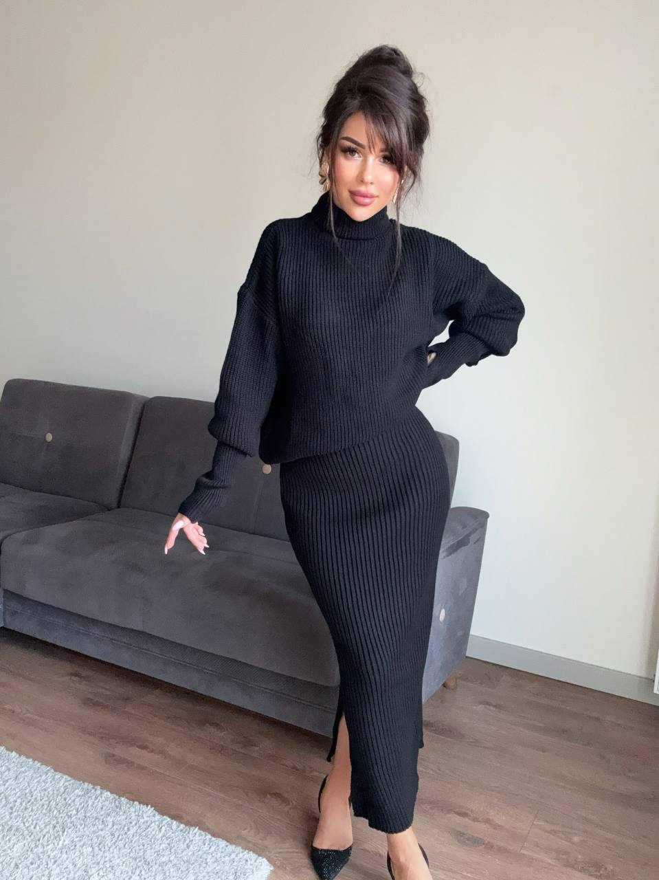Woman in a black outfit standing in a living room with a gray sofa.