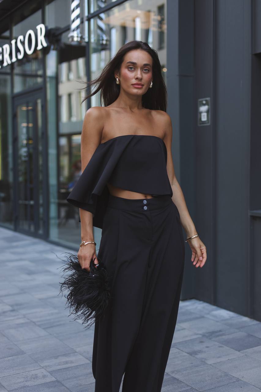 Woman wearing a black strapless top and wide-leg pants on a city street.