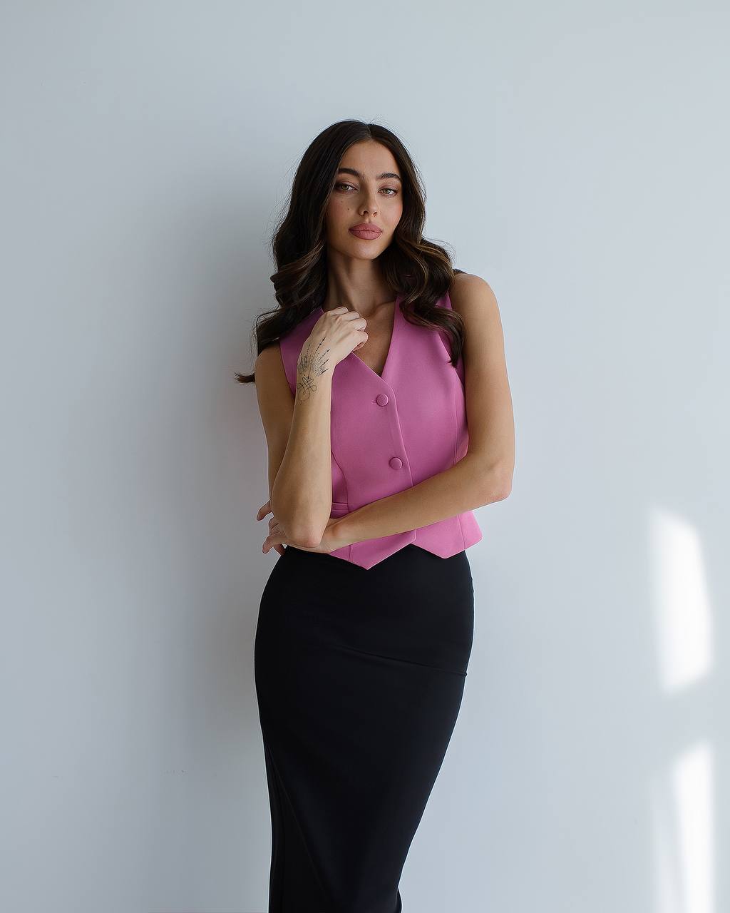 Woman wearing a pink sleeveless top and black pants against a white background