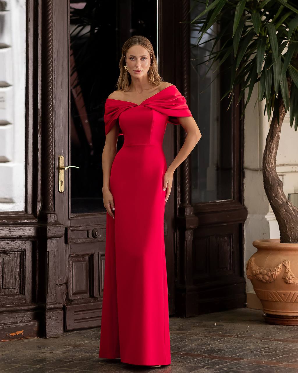 Woman in a red evening gown standing in an elegant indoor setting.