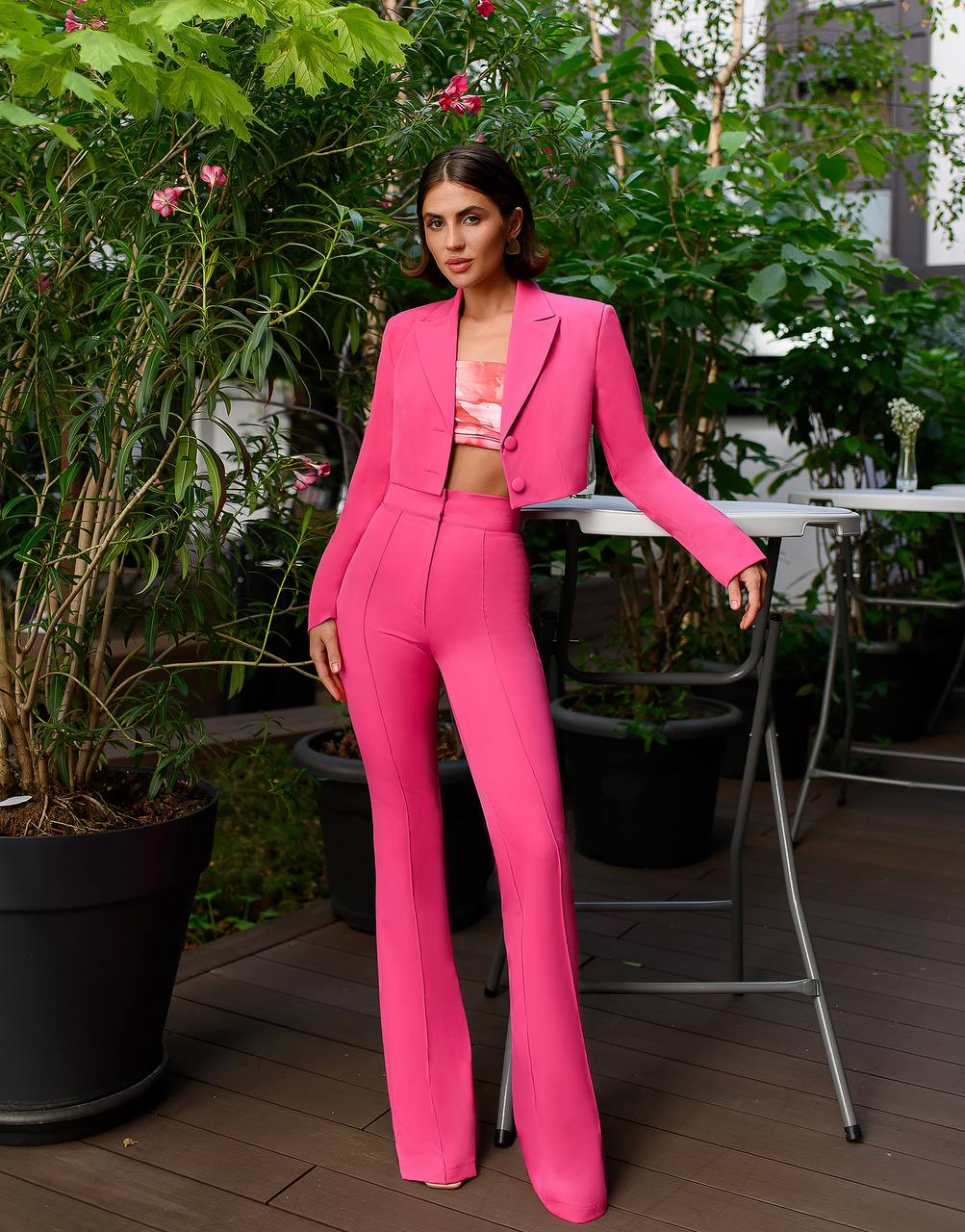 Woman in a bright pink suit standing outdoors with greenery and tables in the background