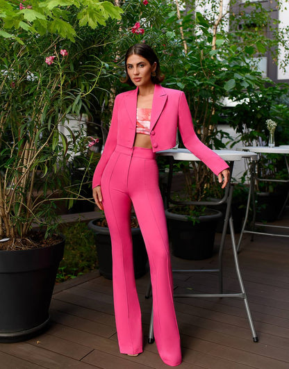 Woman in a bright pink suit standing outdoors with greenery and tables in the background
