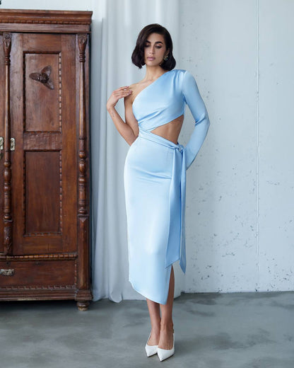 Woman in a light blue dress standing next to a wooden cabinet.