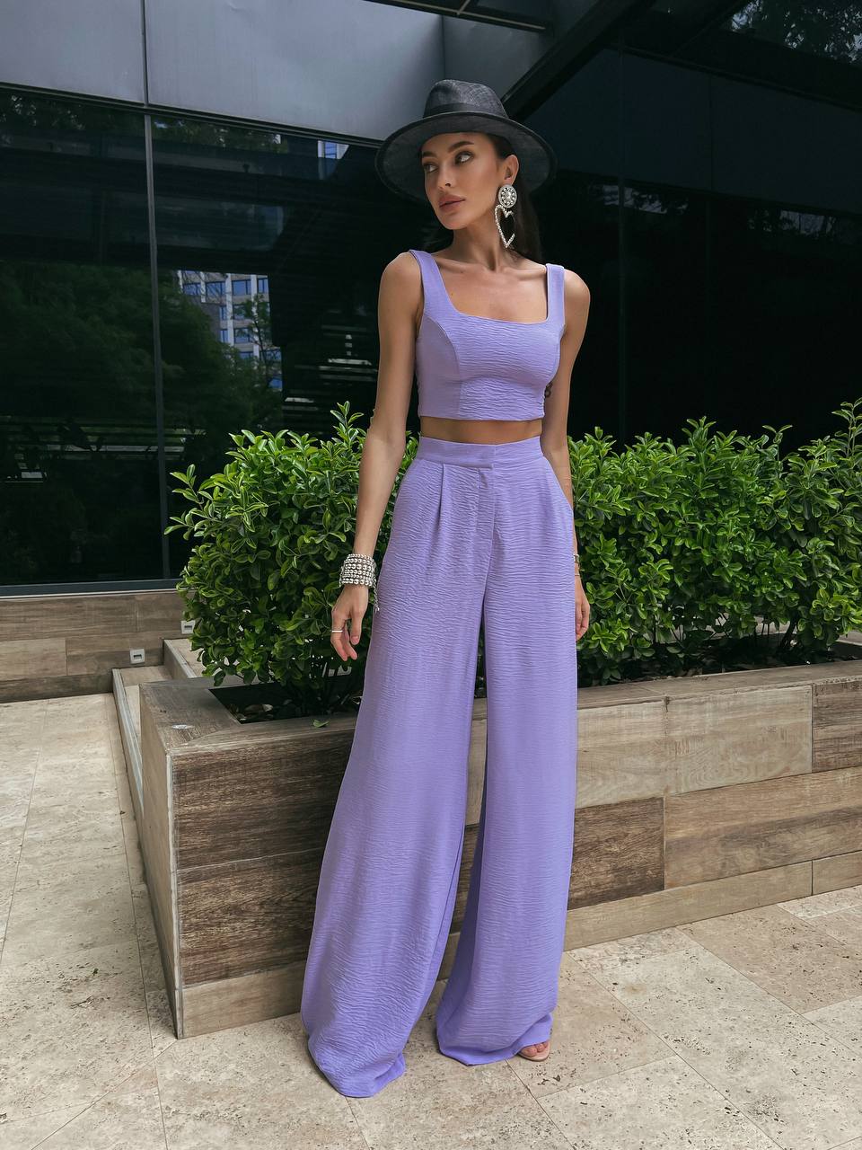 Woman in a lavender outfit standing outdoors with greenery in the background