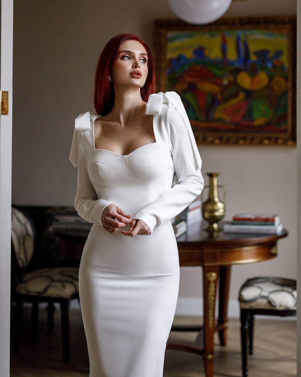 Woman in a white dress standing in an elegant room with a painting in the background