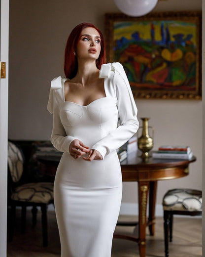 Woman in a white dress standing in an elegant room with a painting in the background