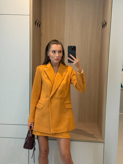 Woman taking a mirror selfie wearing a mustard yellow blazer dress in a store.