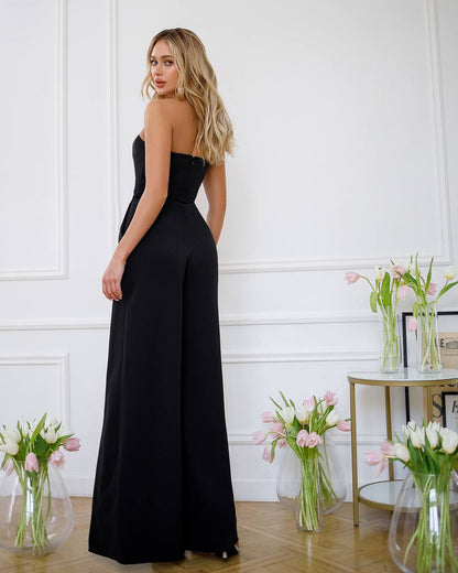 Woman wearing a black strapless jumpsuit standing in a room with decorative elements.