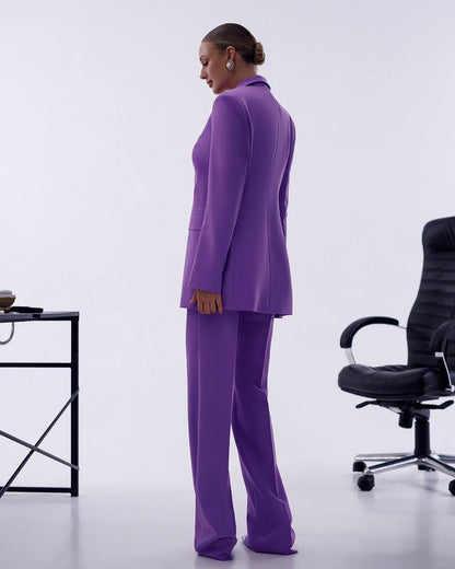 Person wearing a purple suit standing in an office setting with a chair and table.