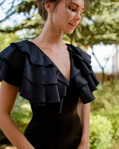 Woman wearing a black ruffled top outdoors with greenery in the background