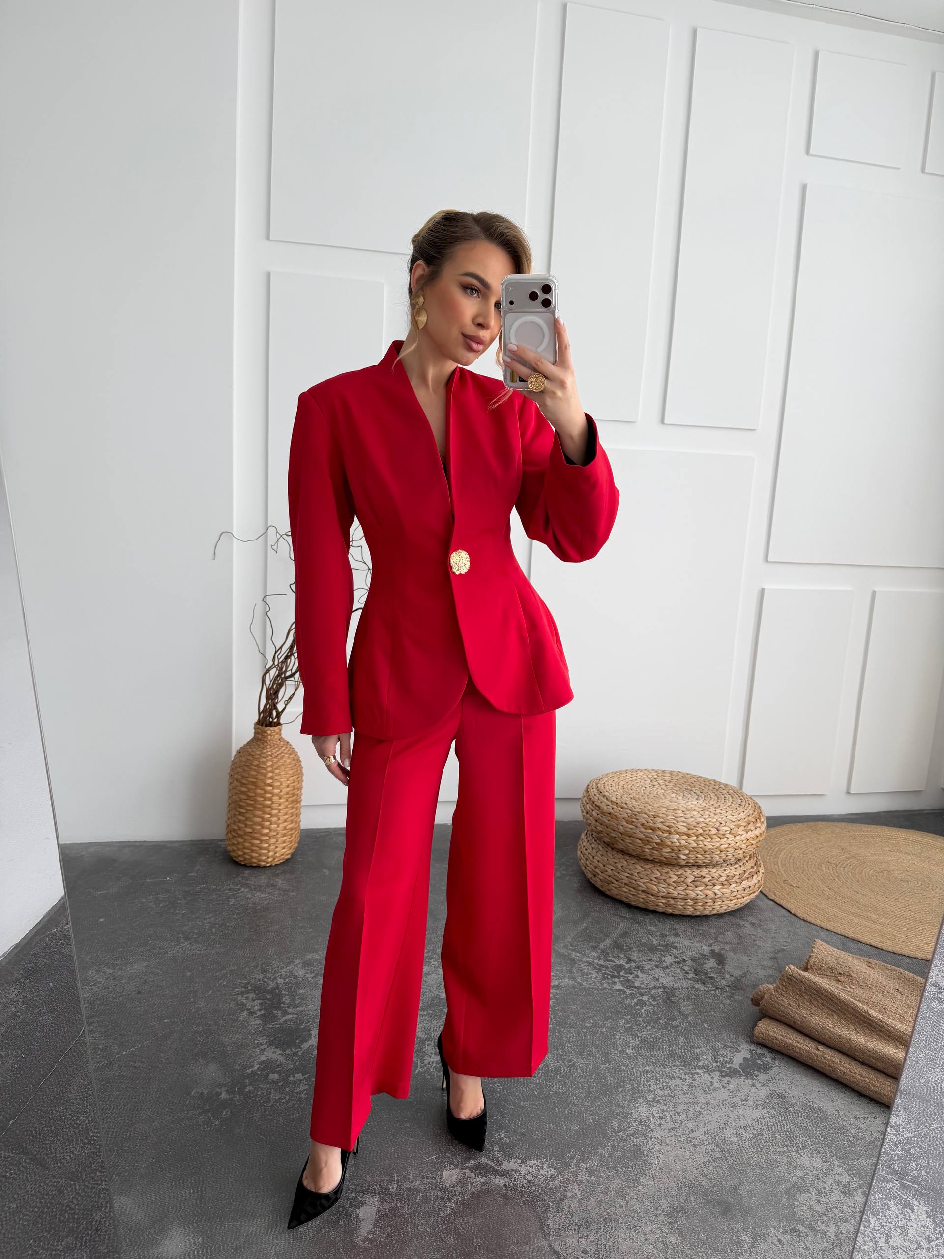 Person wearing a red suit taking a mirror selfie in a minimalistic room.