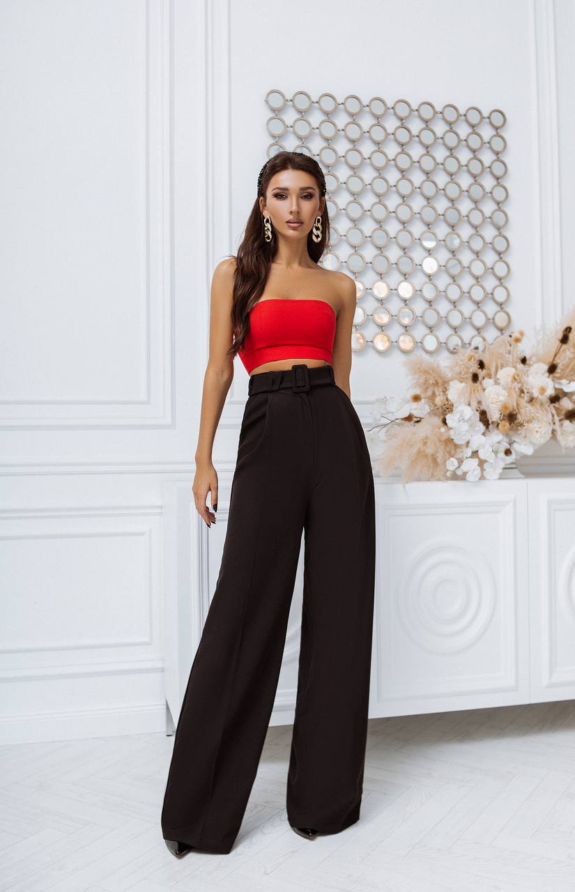 Woman wearing a red strapless top and black wide-leg pants in a stylish interior setting.