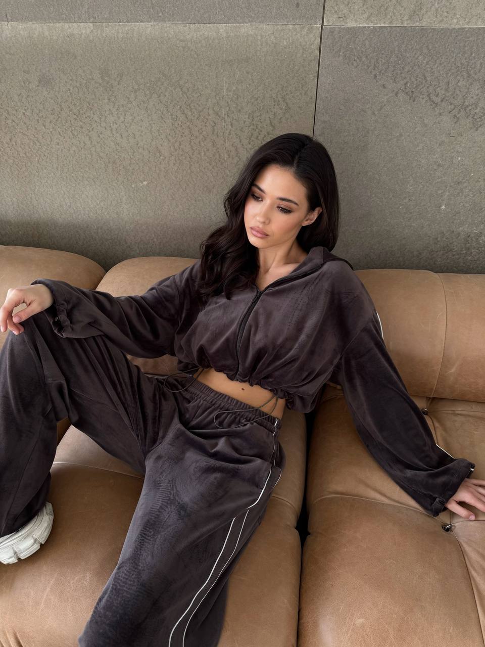 Woman sitting on a brown couch wearing a dark gray outfit.