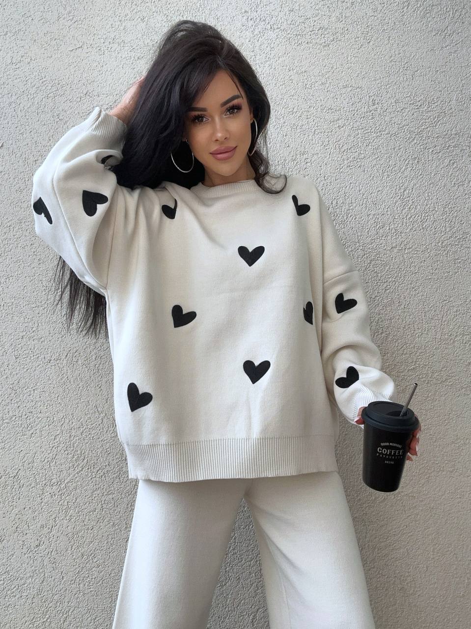 Woman wearing a white sweater with black heart patterns against a plain background