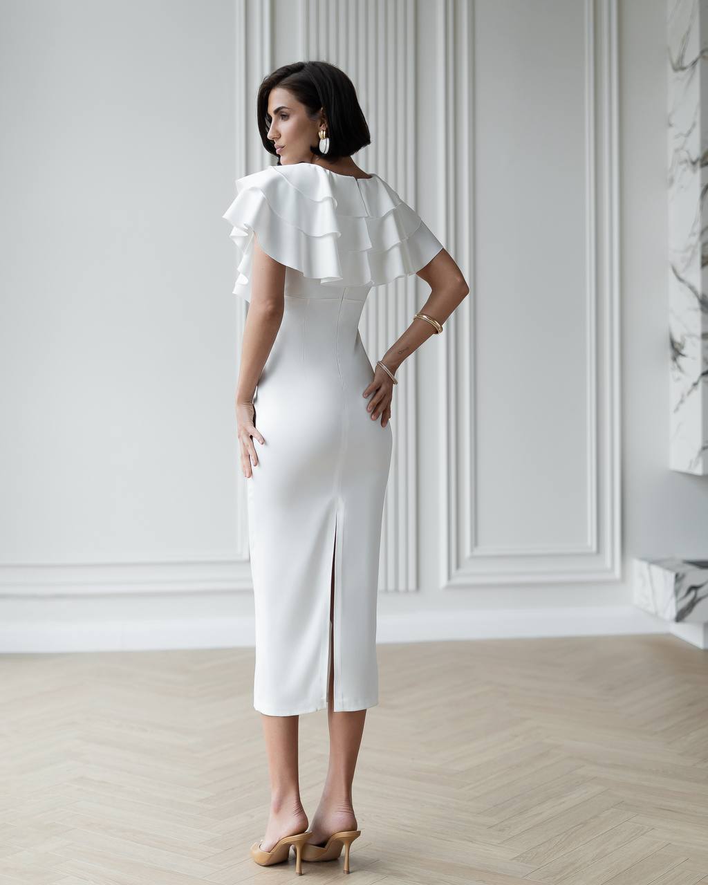 Woman wearing a white dress with ruffled sleeves in an elegant room.