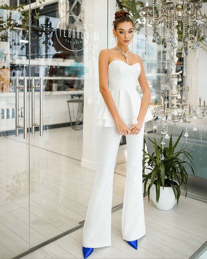 Woman in a white strapless dress with blue shoes standing in a stylish interior setting.