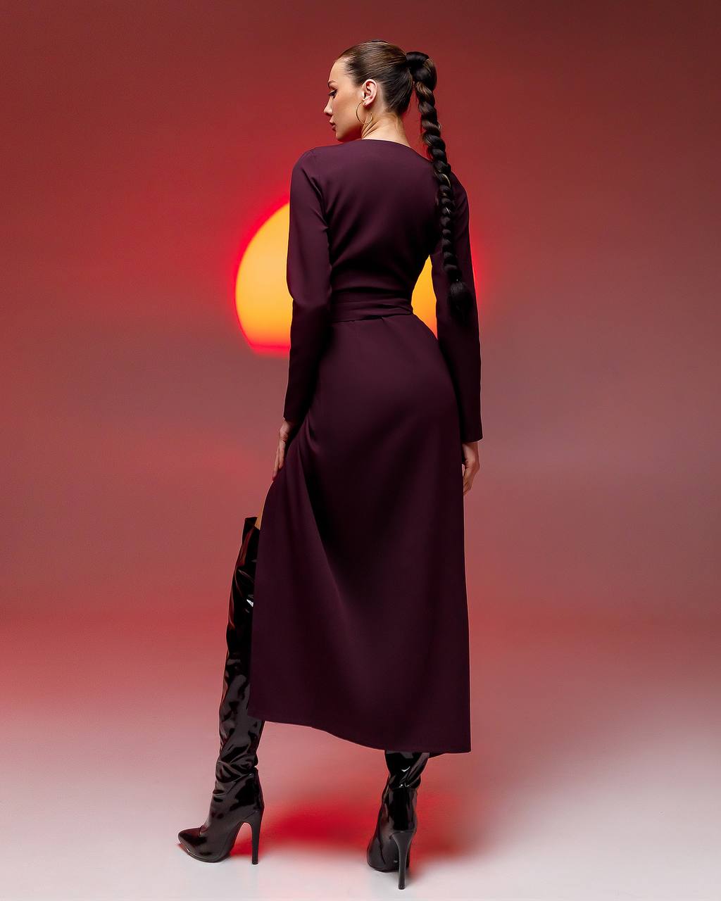 Woman in a long dark dress and high-heeled boots against a red background